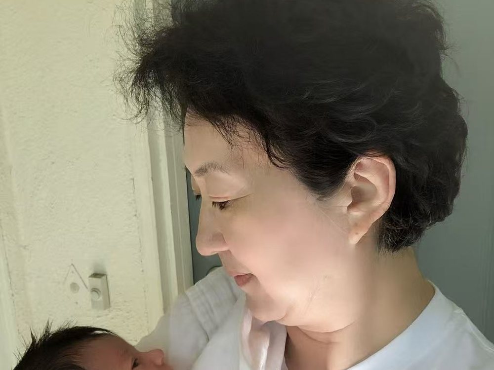 Cathie Li looking down at a sleeping newborn in her arms